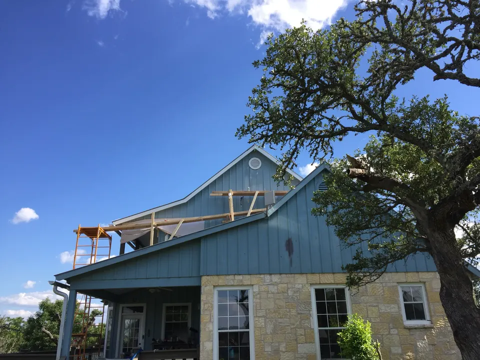 Limestone and blue metal-sided home beneath a Hill Country live oak