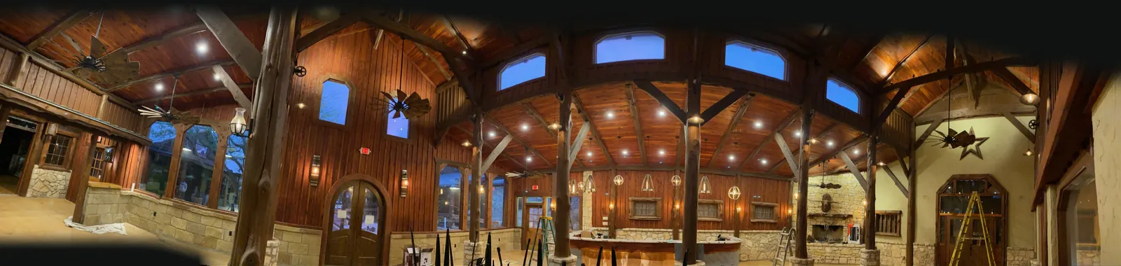 Panorama of a finished timber-frame hall: vaulted, beamed wood ceiling, arched windows, stone wainscot and arched wood doors